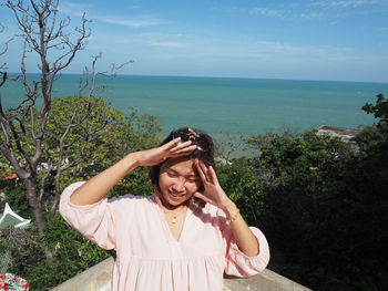 Young woman smiling by sea against sky