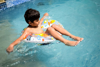 Happy indian boy swimming in a pool, kid wearing swimming costume along with air tube during day