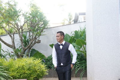 Young man looking away while standing against plants