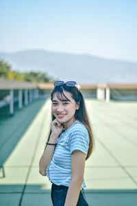 Portrait of smiling young woman standing against sky