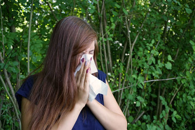 Sick woman wiping her nose against plants