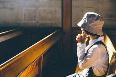 Side view of woman with hands clasped praying in church