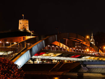 Illuminated bridge by buildings against sky at night