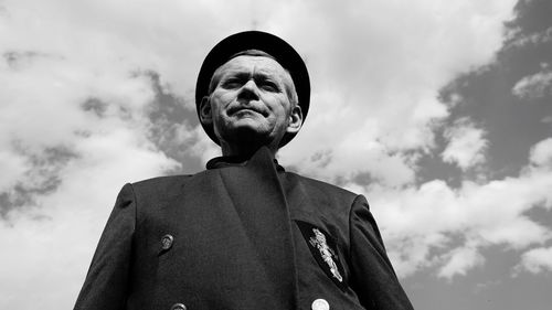 Low angle portrait of senior man wearing suit while standing against sky