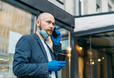 Man holding coffee up talking on phone standing outdoors