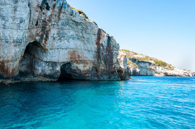 Rock formations by sea against clear blue sky