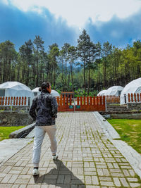 Rear view of woman walking on footpath amidst trees against sky