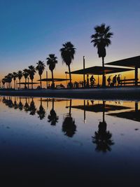 Reflection of palm trees in puddle against sky during sunset