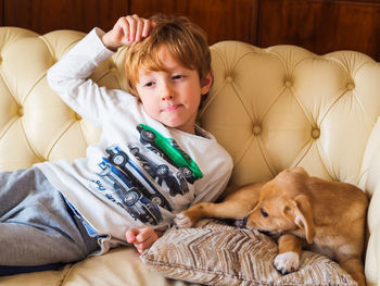 Thoughtful boy resting with dog on sofa at home