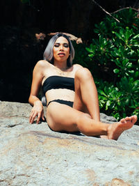 Portrait of young trans woman sitting on rock