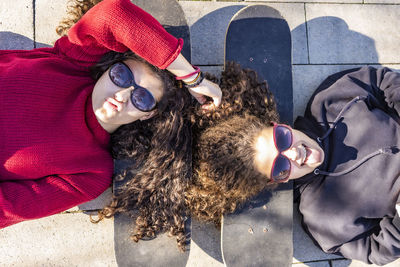 High angle portrait of teenage girls lying with skateboard outdoors