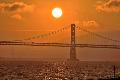 Bridge over sea against orange sky