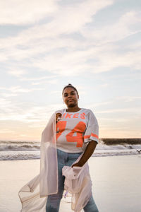 Portrait of young man standing at beach against sky