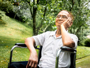 Senior man relaxing on wheelchair against trees