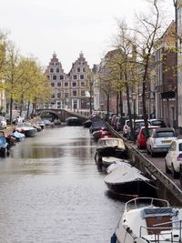 Boats moored in canal by city against sky