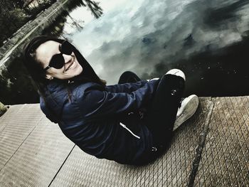 Side view of smiling young woman sitting on footpath by lake