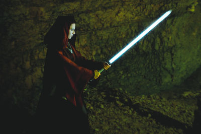 Side view of woman holding sword in cave