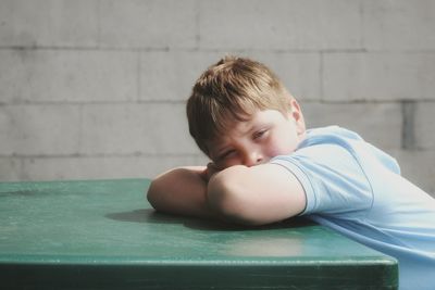 Portrait of boy lying down on table against wall