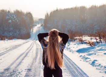 Rear view of woman with long blond hair standing on snow covered road