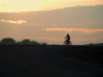 Silhouette man riding bicycle against sky during sunset