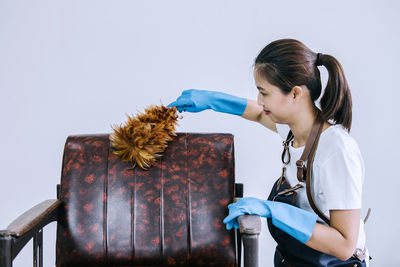 Side view of woman cleaning chair against white background
