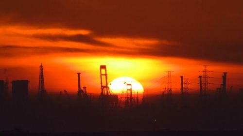 Silhouette electricity pylons against sky during sunset