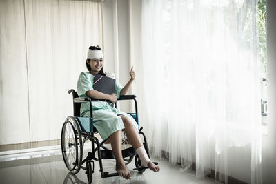 Woman with bandaged head and leg gesturing while sitting on wheelchair hospital