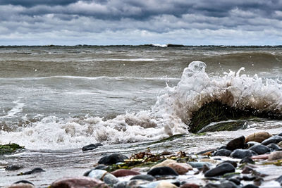 Waves splashing on rocks at shore against sky