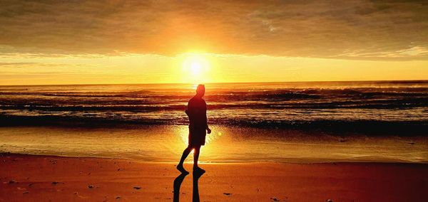 Man standing on beach against sky during sunset