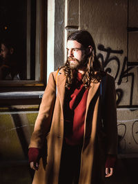 Young man looking away while standing against wall