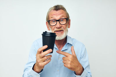 Portrait of senior man showing coffee cup against white background