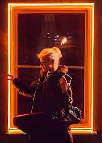 Woman sitting by illuminated window
