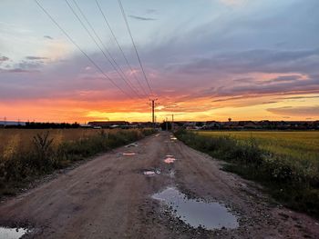 Road amidst field against sky during sunset