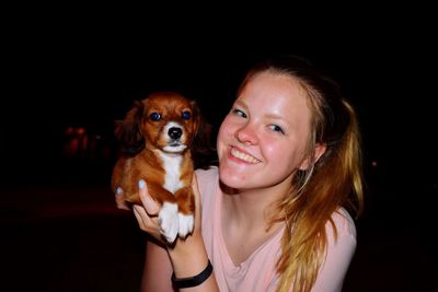 Portrait of smiling woman with dog against black background