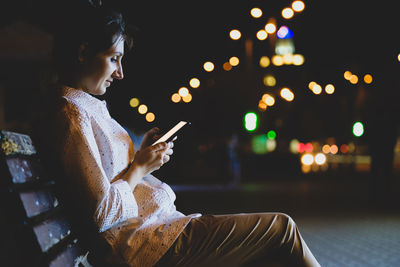 Side view of young woman looking away while sitting at night