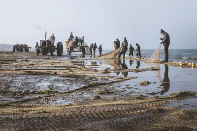 People working on shore at beach against sky