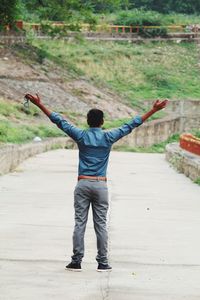 Rear view of man with arms raised standing on road