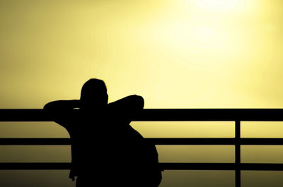 Silhouette man standing by railing against clear sky