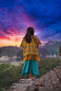 Rear view of woman standing at temple against sky during sunset