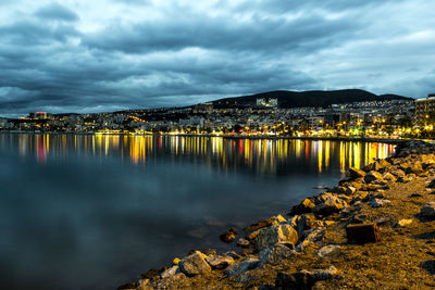 Illuminated bridge over river by city against sky