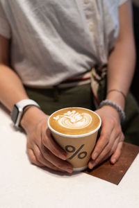 Midsection of woman holding coffee cup on table