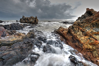 Long exposure image of waves crashing at beach against storm clouds