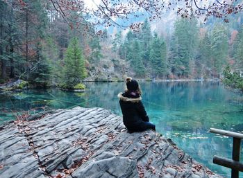 Rear view of woman sitting by lake in forest