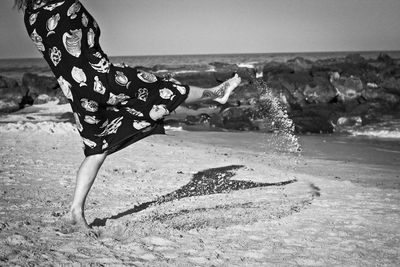 Low section of woman kicking sand at beach against sky