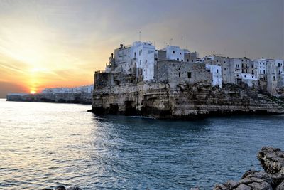 Buildings in sea against sky during sunset