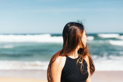 Rear view of woman standing at beach against sky