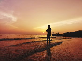 Silhouette man standing on shore at beach against sky during sunset