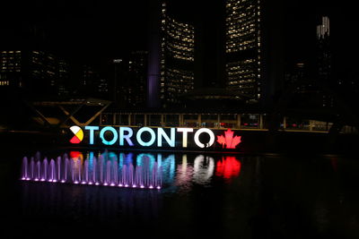 Illuminated text by river in city at night