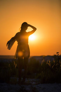 Silhouette woman standing on field against orange sky