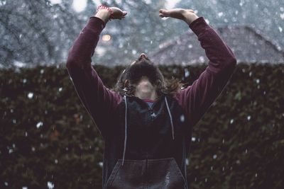 Man standing against hedge during snow fall